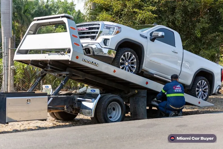 Flatbed tow truck loading a junk car for removal in a Miami neighborhood