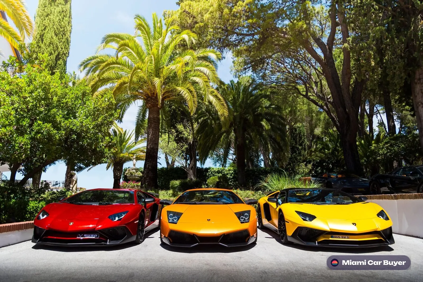 Yellow and orange Lamborghinis parked beneath Miami palm trees, representing the full range of cars sold through Miami Car Buyer across the county