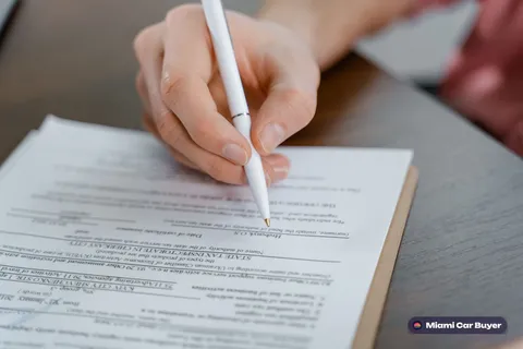 Person signing a car title document with car keys and cash nearby in Miami