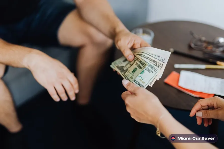 Close-up of a hand exchanging cash and car keys during a car sale transaction in Miami