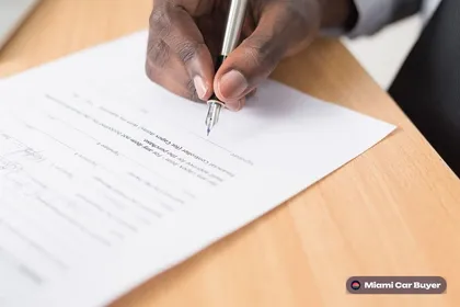 Close-up of a hand signing a written offer document with car keys on the table